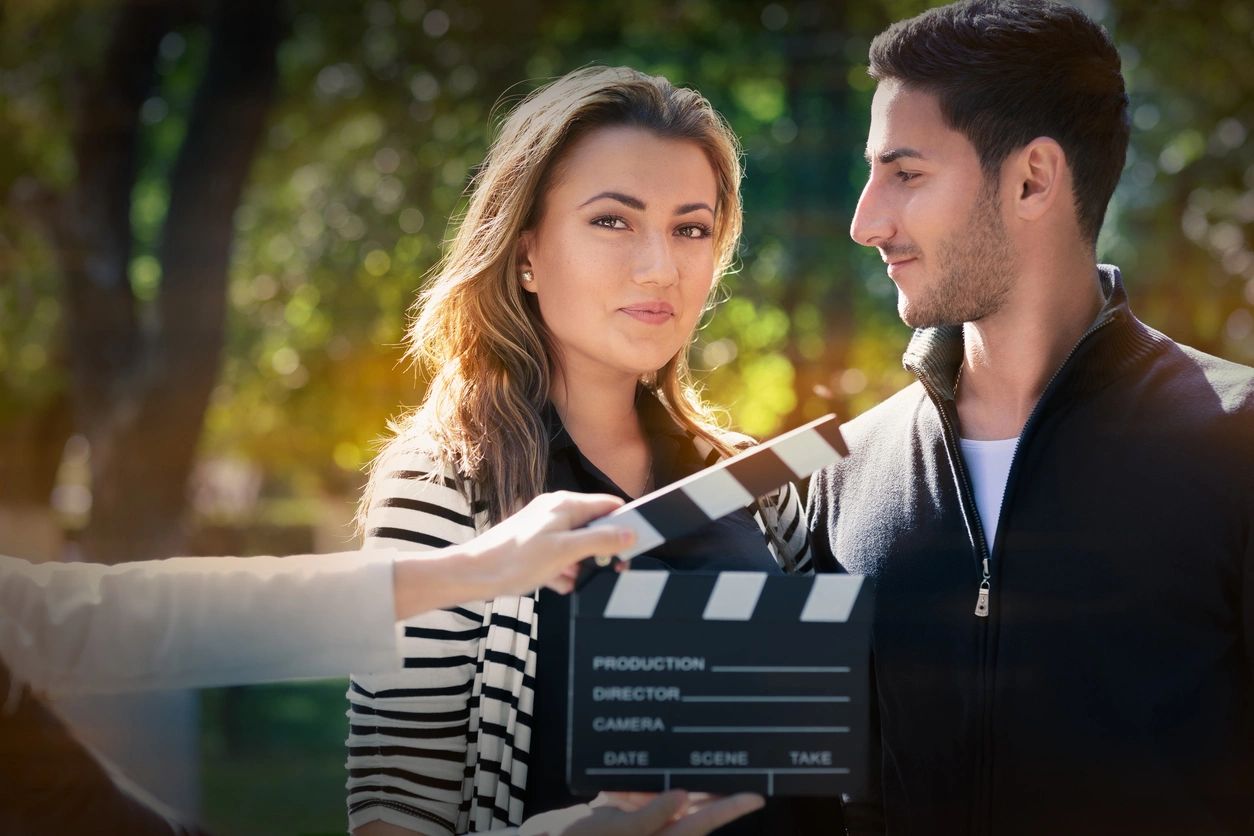 A woman holding a movie clapper board next to a man.